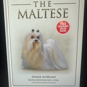 May include: A book titled "THE MALTESE" with a white Maltese dog on the cover. The book includes the text "Discover a whole new world of dogs" and "FREE TRAINING DVD INSIDE". The author is Diane Morgan, with Wayne Hunthausen, D.V.M., as Consulting Veterinary Editor.
