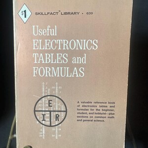 May include: A vintage book titled "Useful Electronics Tables and Formulas" with the text "Skillfact Library" and a price tag of $1. The cover is a light brown color with white text and a circular graphic.