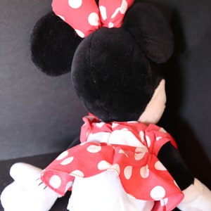 Pu&ograve; includere: Un giocattolo di peluche a forma di topo dei cartoni animati con pelliccia nera, grandi orecchie e un fiocco rosso con pois bianchi. Il topo indossa un vestito rosso con pois bianchi.