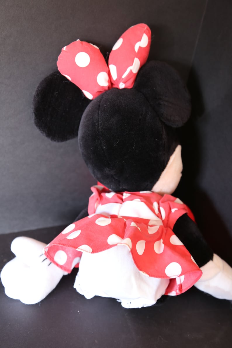 Pu&ograve; includere: Un giocattolo di peluche a forma di topo dei cartoni animati con pelliccia nera, grandi orecchie e un fiocco rosso con pois bianchi. Il topo indossa un vestito rosso con pois bianchi.