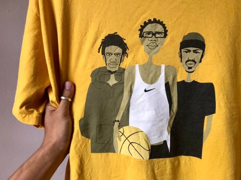 May include: Yellow t-shirt with a graphic print of three cartoon men. The men are wearing different outfits, including a white tank top with a Nike logo, a green hooded sweatshirt, and a black t-shirt. The men are holding a basketball.