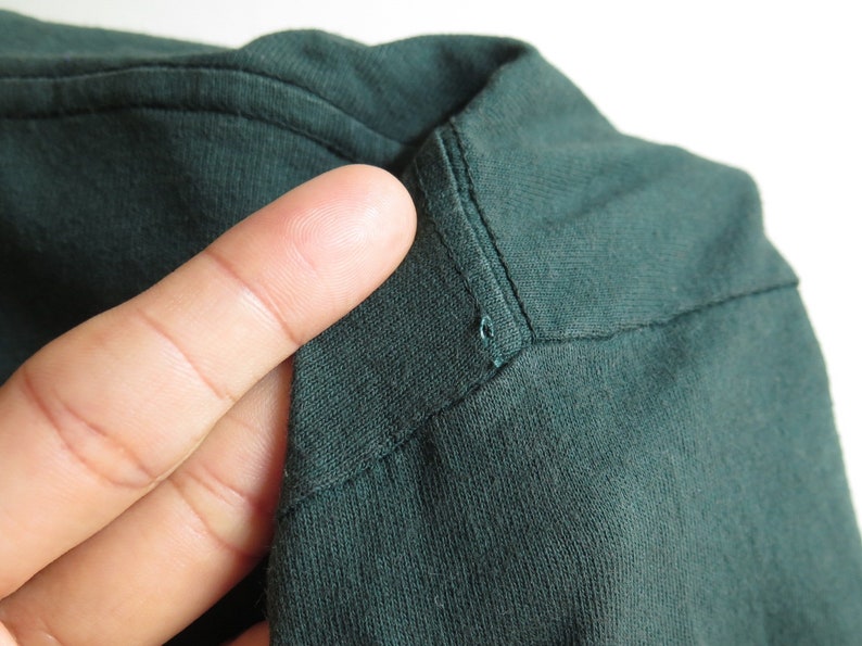 May include: Close-up of the dark green fabric of a shirt, showing the stitching detail at the neckline.