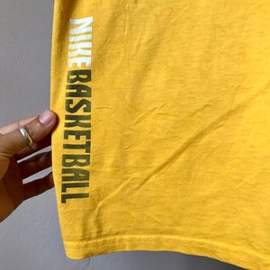 May include: Yellow t-shirt with the text "NIKE BASKETBALL" printed on the left side in white and green letters.