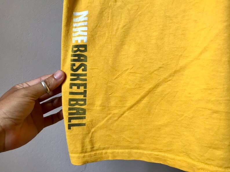 May include: Yellow t-shirt with the text "NIKE BASKETBALL" printed on the left side in white and green letters.