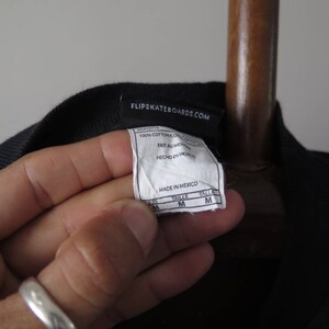 May include: Black t-shirt with a white tag that says "Flip Skateboards.com" and includes details about the fabric and size. The tag also says "Made in Mexico".