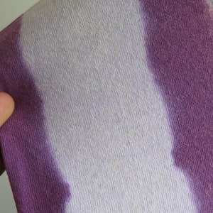 May include: Close-up of a tie-dye fabric with white, purple and green stripes. The fabric has a soft, textured feel.