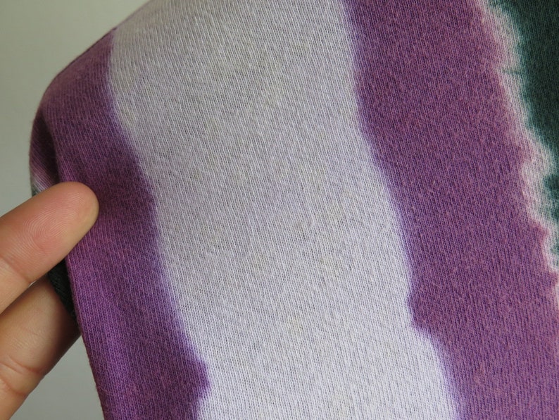May include: Close-up of a tie-dye fabric with white, purple and green stripes. The fabric has a soft, textured feel.