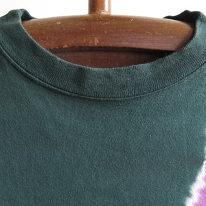 May include: A dark green t-shirt with a tie-dye pattern in shades of white and purple.