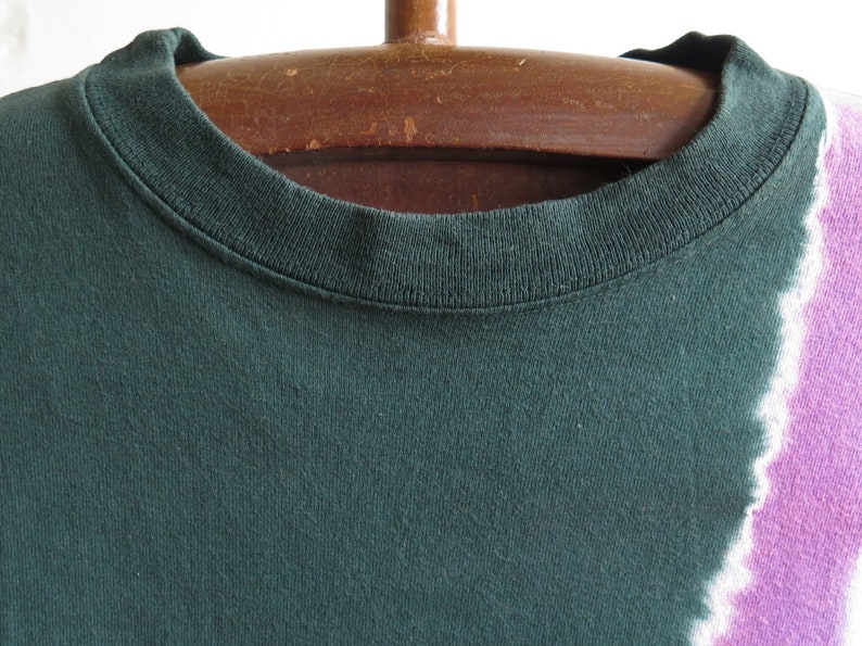 May include: A dark green t-shirt with a tie-dye pattern in shades of white and purple.