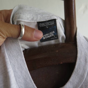 May include: A white t-shirt with a black tag that says "Gildan Screen Stars" and "Styled in USA". The tag also shows the size "L" and the fabric composition: 90% cotton, 10% polyester.
