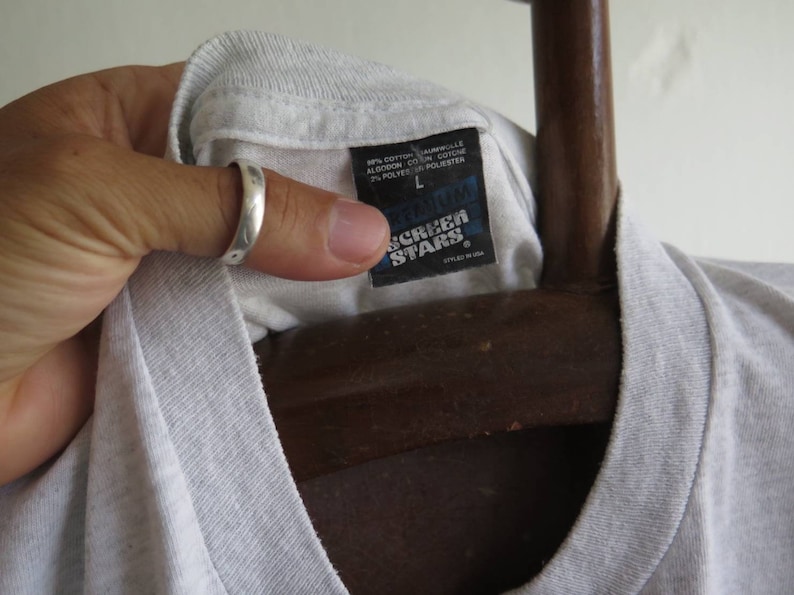 May include: A white t-shirt with a black tag that says "Gildan Screen Stars" and "Styled in USA". The tag also shows the size "L" and the fabric composition: 90% cotton, 10% polyester.