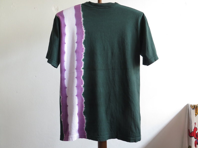 May include: A green short-sleeved t-shirt with a white and purple tie-dye pattern on the left side.