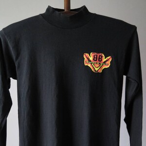 Op de afbeelding: Zwart longsleeve shirt met een mock neck. Het shirt heeft een gele, oranje en rode grafische afbeelding van een gestileerde '88' met de tekst 'Buick Boy' eronder.