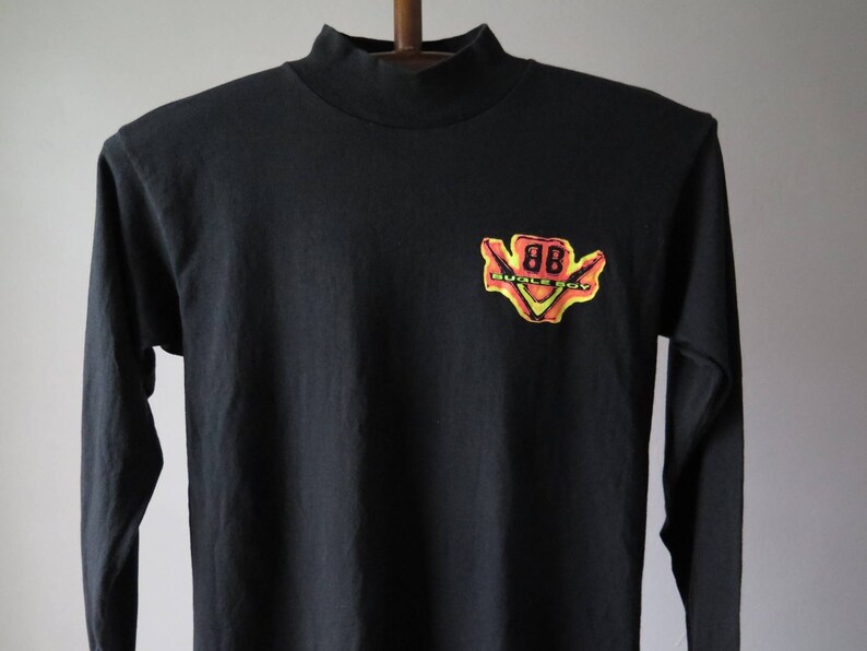 Op de afbeelding: Zwart longsleeve shirt met een mock neck. Het shirt heeft een gele, oranje en rode grafische afbeelding van een gestileerde '88' met de tekst 'Buick Boy' eronder.