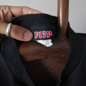 May include: Black t-shirt with a black and red "FLIP" label attached to the neck.