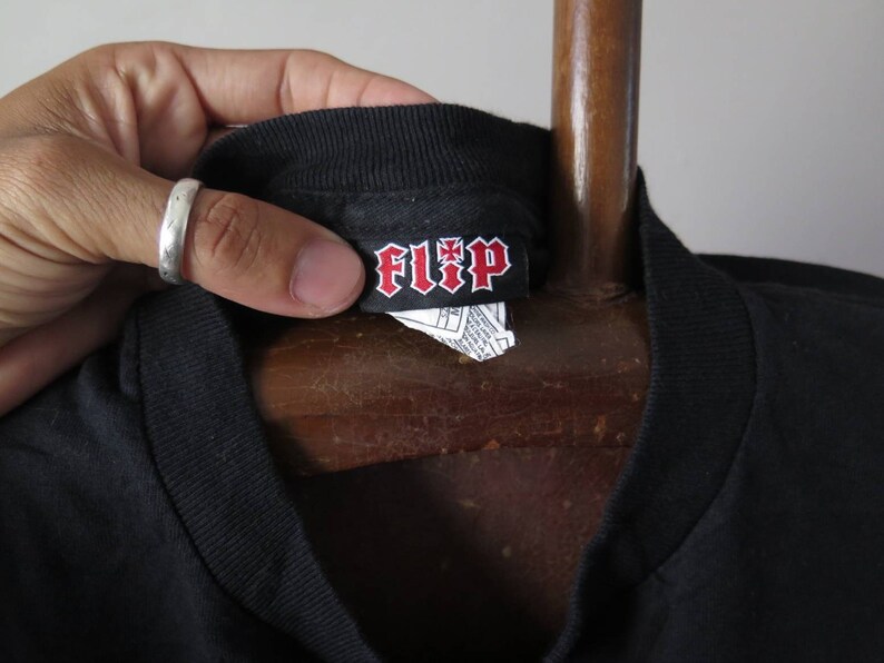 May include: Black t-shirt with a black and red "FLIP" label attached to the neck.