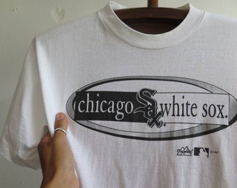 May include: White t-shirt with a black and white graphic of the Chicago White Sox logo. The logo is inside an oval with the words "Chicago White Sox" printed on it. The shirt has a Majestic logo and the copyright year 1997 printed on the bottom.