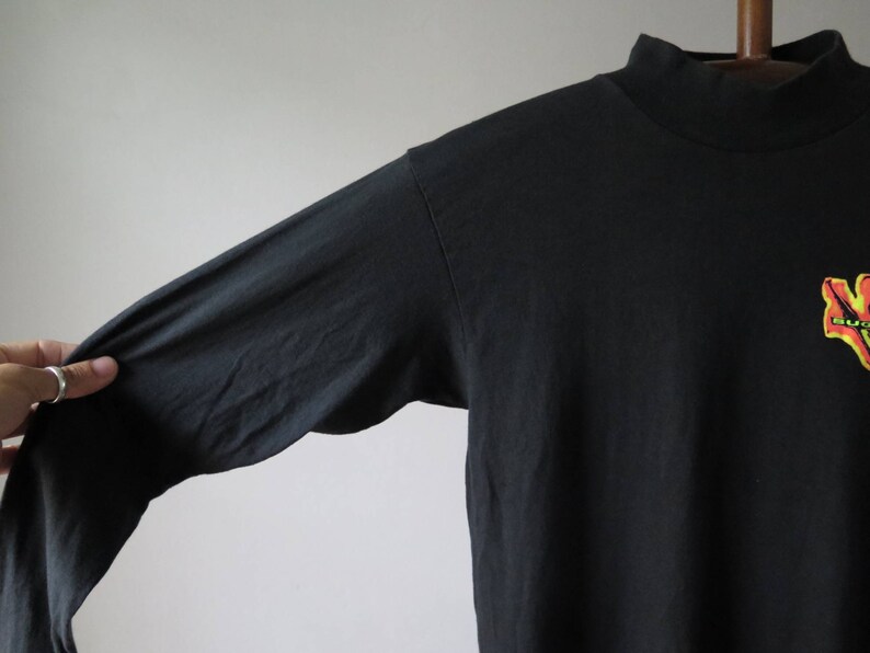 Op de afbeelding: Zwart longsleeve shirt met een mock neck en een kleurrijke afbeelding op de voorkant.
