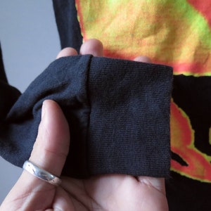 Op de afbeelding: Zwart shirt met lange mouwen met een kleurrijk tie-dye patroon. Het shirt heeft een geribbelde manchet.