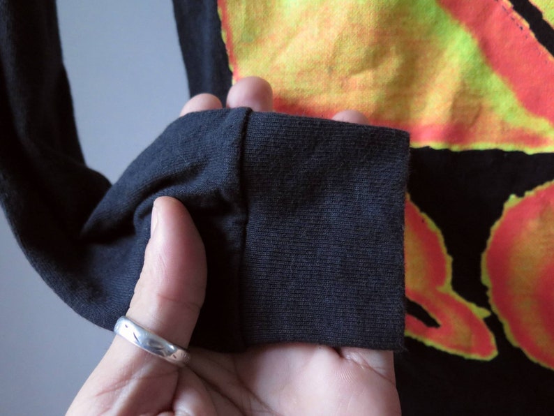 Op de afbeelding: Zwart shirt met lange mouwen met een kleurrijk tie-dye patroon. Het shirt heeft een geribbelde manchet.