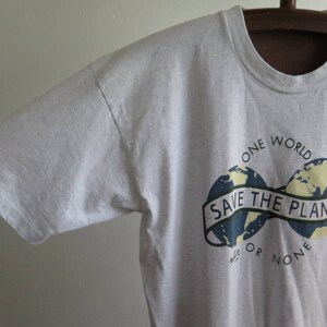 May include: Gray t-shirt with a graphic of two blue and yellow globes with the text "One World Save The Planet Or None".