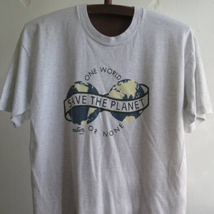 May include: A gray t-shirt with a graphic of two globes connected by a banner that reads "Save the Planet". The text "One World" is above the globes and "natura_ or none" is below.