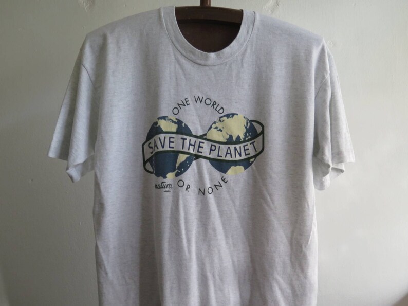 May include: A gray t-shirt with a graphic of two globes connected by a banner that reads "Save the Planet". The text "One World" is above the globes and "natura_ or none" is below.