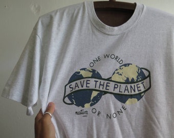 May include: A gray t-shirt with a graphic of two blue and yellow globes with the text "One World Save The Planet Natura Or None" printed on it.