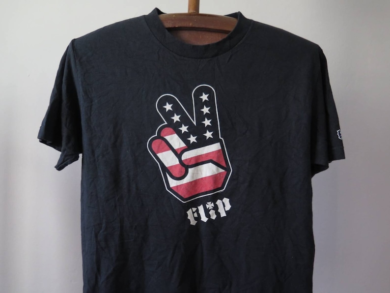 May include: Black t-shirt with a red, white, and blue peace sign graphic and the word "FLIP" printed below it.