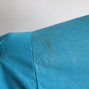 May include: Close-up of a teal blue t-shirt with a slight stain on the shoulder.