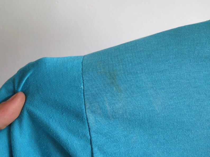 May include: Close-up of a teal blue t-shirt with a slight stain on the shoulder.