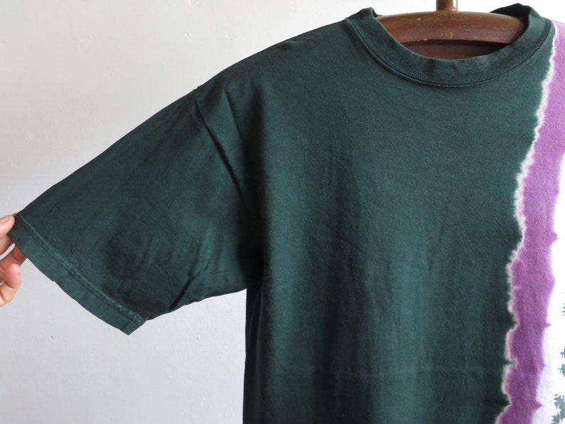 May include: A dark green t-shirt with a purple and white tie-dye design on the right side.