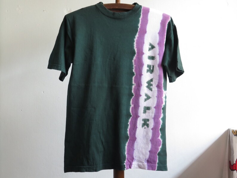 May include: A green t-shirt with a purple and white tie-dye design on the right side. The design features the word "Airwalk" in a stylised font.