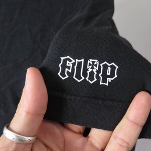 May include: Black t-shirt with a white "FLIP" logo in a gothic font.
