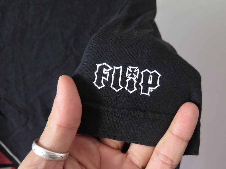 May include: Black t-shirt with a white "FLIP" logo in a gothic font.