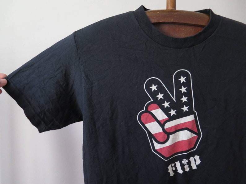 May include: Black t-shirt with a peace sign graphic featuring the American flag colors. The word "Flip" is printed below the graphic.