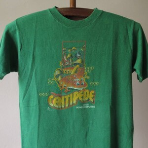 May include: Green t-shirt with a vintage Atari Centipede video game graphic. The graphic features a cartoon centipede with mushrooms and the text "Centipede Atari Home Computers".