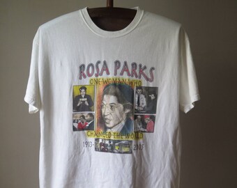 May include: White t-shirt featuring a graphic of Rosa Parks with the text "ROSA PARKS ONE WOMAN WHO CHANGED THE WORLD" and the years 1913-2005. The design includes portraits and images related to her life and legacy.