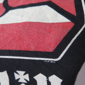 May include: Black t-shirt with a red, white, and black graphic design. The graphic features a stylized hand with a cross and the text "FLIP 2010".