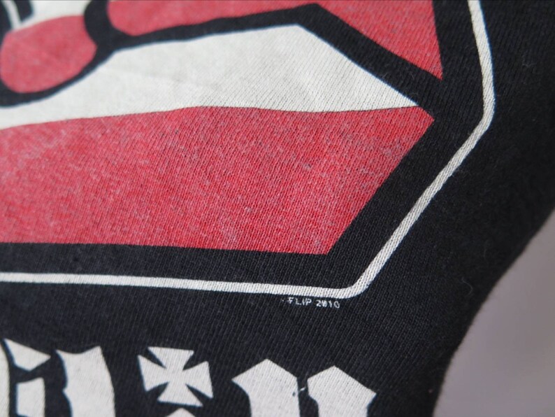 May include: Black t-shirt with a red, white, and black graphic design. The graphic features a stylized hand with a cross and the text "FLIP 2010".
