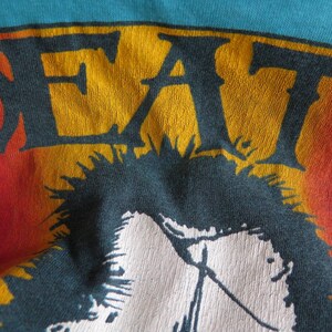 May include: A vintage t-shirt with a faded rainbow design and the word "DEAF" in yellow and orange letters. The shirt features a black and white graphic of a person with spiky hair.