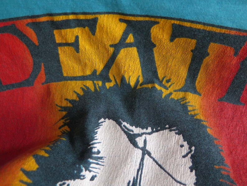 May include: A vintage t-shirt with a faded rainbow design and the word "DEAF" in yellow and orange letters. The shirt features a black and white graphic of a person with spiky hair.