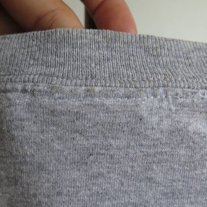 Pu&ograve; includere: Primo piano del collo di una maglietta grigia. Il collo &egrave; a costine e presenta una cucitura doppia.