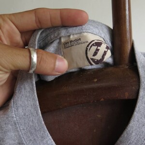 Pu&ograve; includere: Maglietta grigia con un'etichetta che recita "Dirt McGirt, Fashion Industry, Trademark Lifestyle Co."