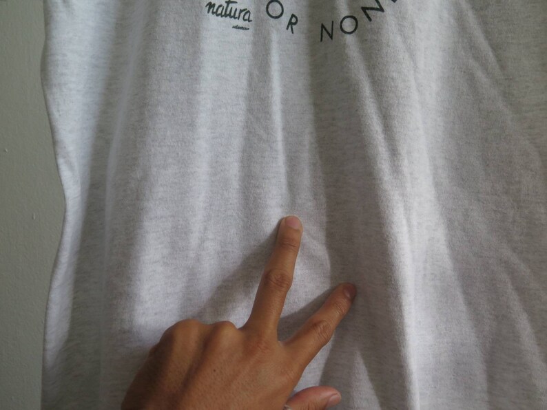 May include: A close-up of a gray t-shirt with the text "natura OR NON" printed on the front.
