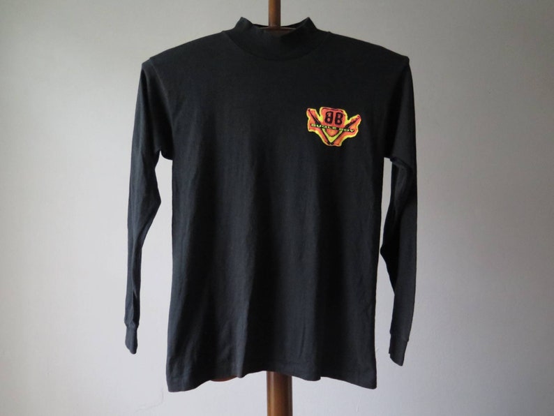 Op de afbeelding: Zwart longsleeve shirt met een mock neck en een gele, oranje en rode afbeelding van een auto met het nummer "88" erop.