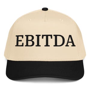 May include: A beige baseball cap with a black brim and the word "EBITDA" embroidered in black block letters across the front. The cap has a curved bill and a black button on top.