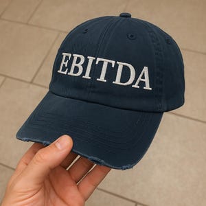 May include: A dark blue baseball cap with a white embroidered logo that says "EBITDA". The cap has a distressed look with frayed edges.