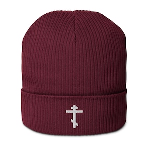 May include: A burgundy ribbed beanie with a white embroidered Orthodox cross. The hat is made of a soft, knitted material and has a folded cuff. The cross is centered on the cuff.