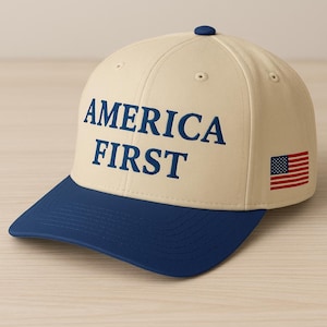 May include: A baseball cap with a cream-colored crown and a navy blue brim. The text "AMERICA FIRST" is embroidered on the front in navy blue, with a small American flag on the side.